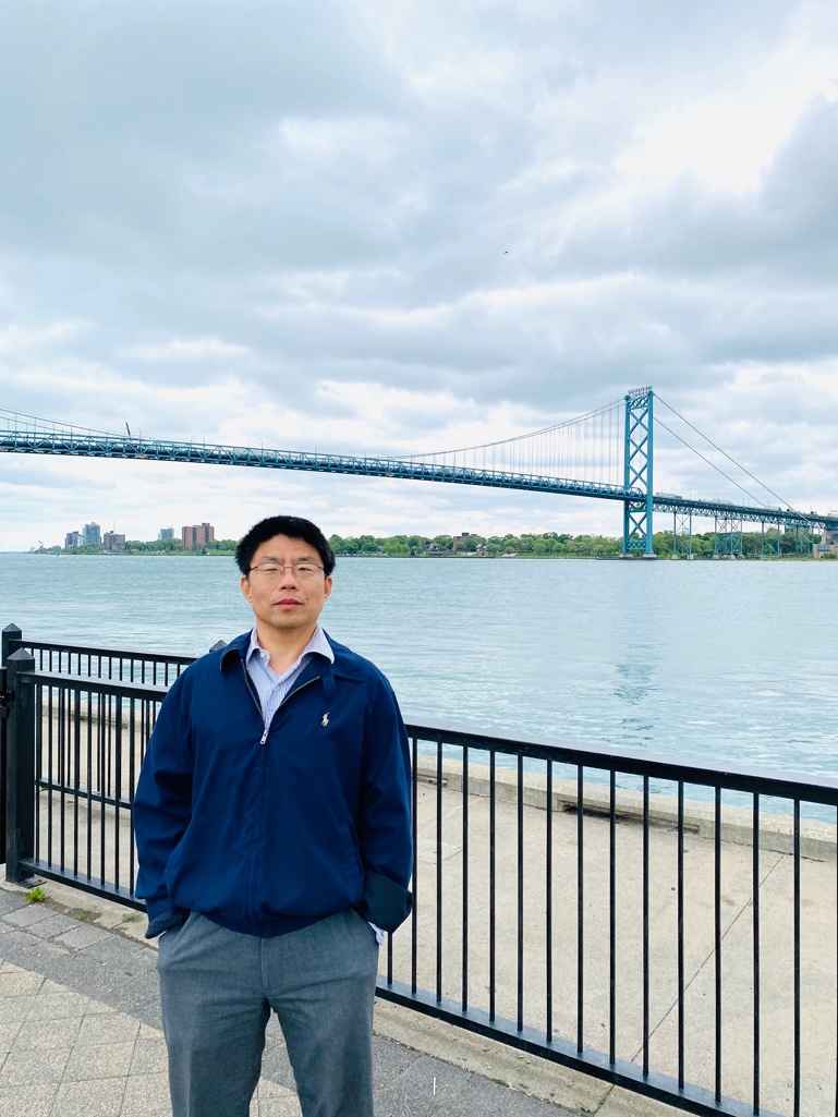 A person standing on a sidewalk by a railing with a bridge in the background
Description automatically generated